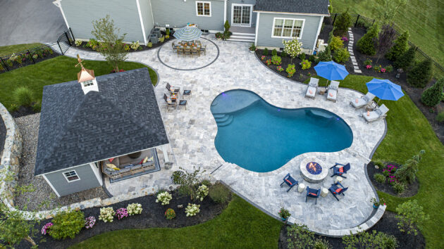 Drone view of Dex by Terra pool design-build project with gas fire pit, pergola, dining patio, and walkways in Norfolk, MA.