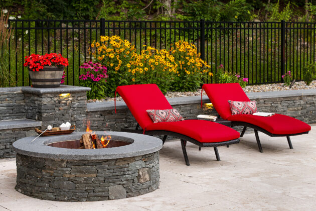 Pool chairs by the stone fire pit and seating wall with s'mores. Dex by Terra Hardscaping & Landscaping project in Sterling Massachusetts.