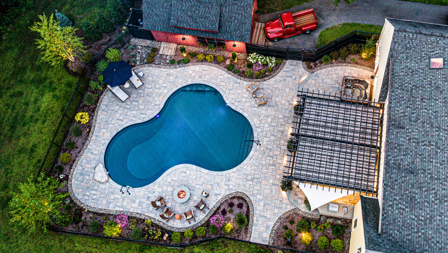 Drone view of hardscape project with pool, fire pit, & outdoor kitchen. Landscape design-build by Dex by Terra in Stow, MA.