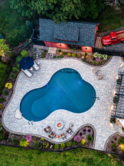 Drone view of hardscape project with pool, fire pit, & outdoor kitchen. Landscape design-build by Dex by Terra in Stow, MA.