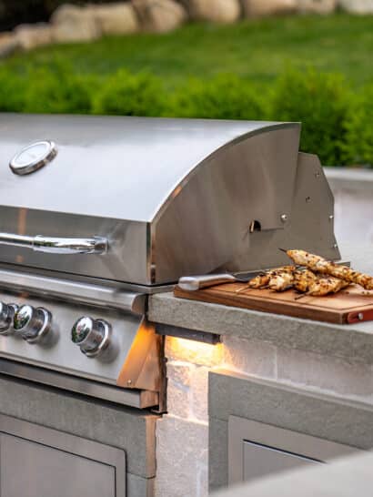 An outdoor kitchen with stainless steel grill and freshly prepared grilled chicken with red wine.