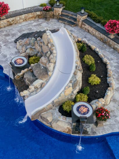 A custom Dex by Terra waterslide with a landscaping bed and water/fire features built with natural stone boulders.