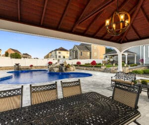 A view of the natural stone paver pool deck from under the pool deck patio pergola. Dex by Terra hardscaping project in Grafton, MA.