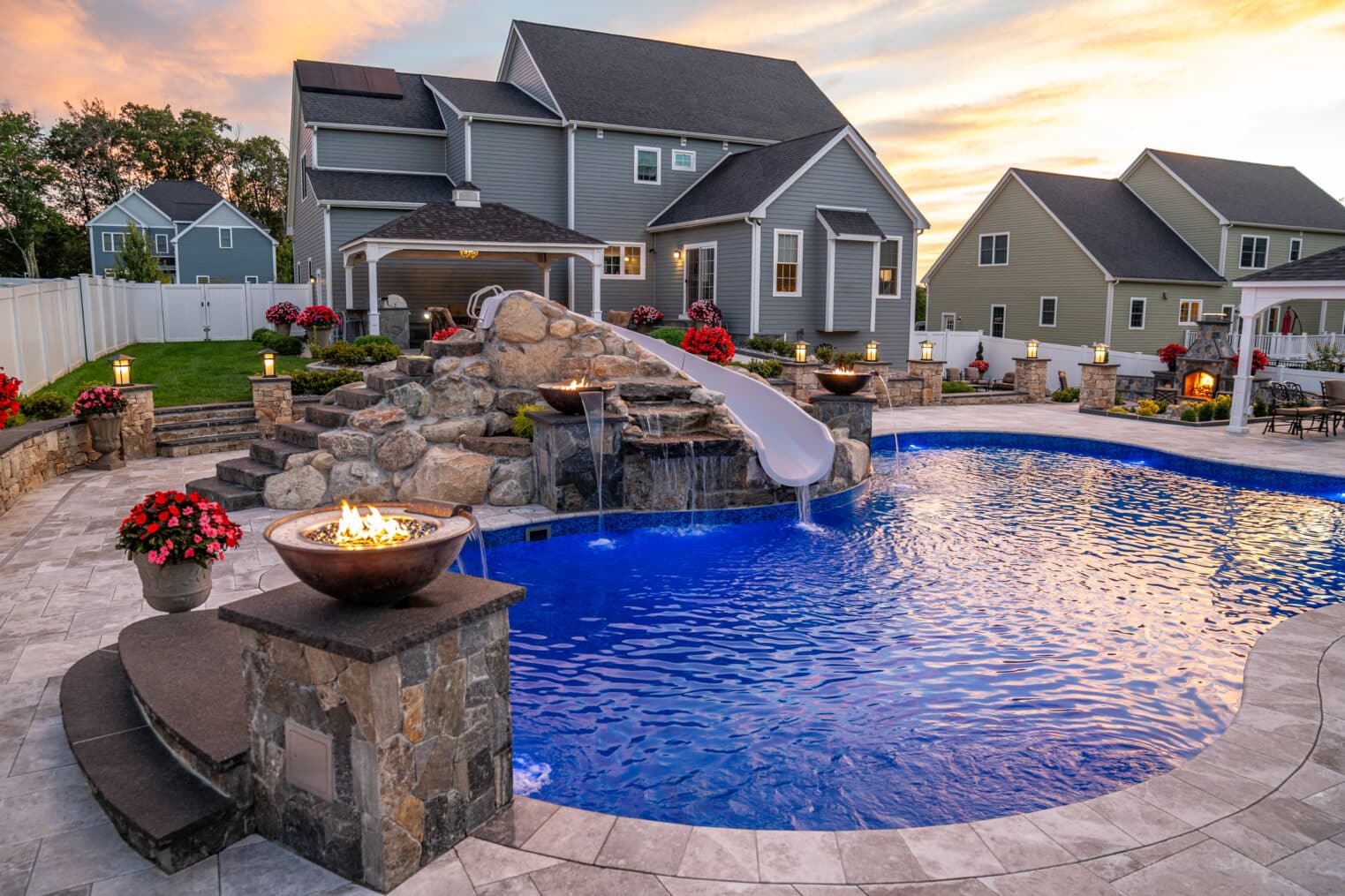 A backyard in Grafton, Massachusetts with a pool deck, waterslide, and fire and water features all built by Dex by Terra.