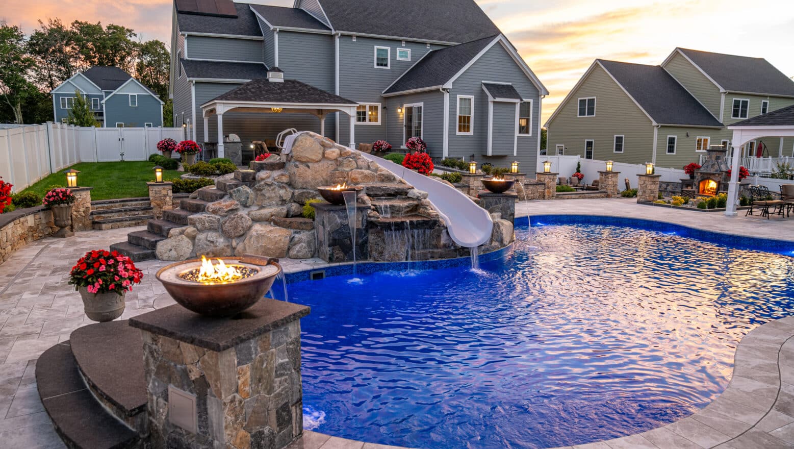 A backyard in Grafton, Massachusetts with a pool deck, waterslide, and fire and water features all built by Dex by Terra.
