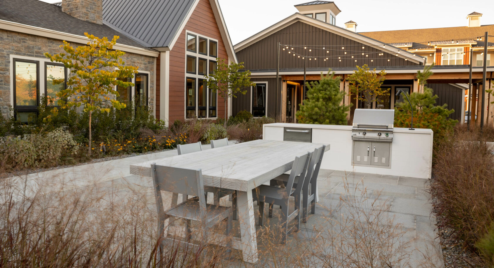 Dining area with table, chairs, and outdoor kitchen at a luxury apartment complex. Dex by Terra Hardscape project in MA.