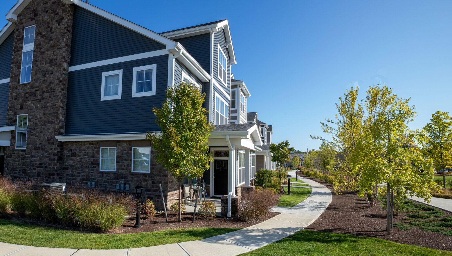 Landscaping with concrete walkways & stone veneer at luxury apartments in MA. Landscape & hardscape work by Dex by Terra.