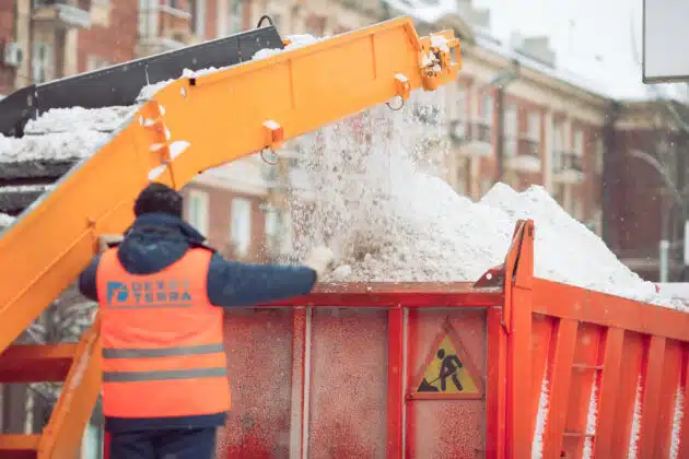 Dex by Terra worker loading snow into dump truck at a commercial snow removal job site with a conveyor.